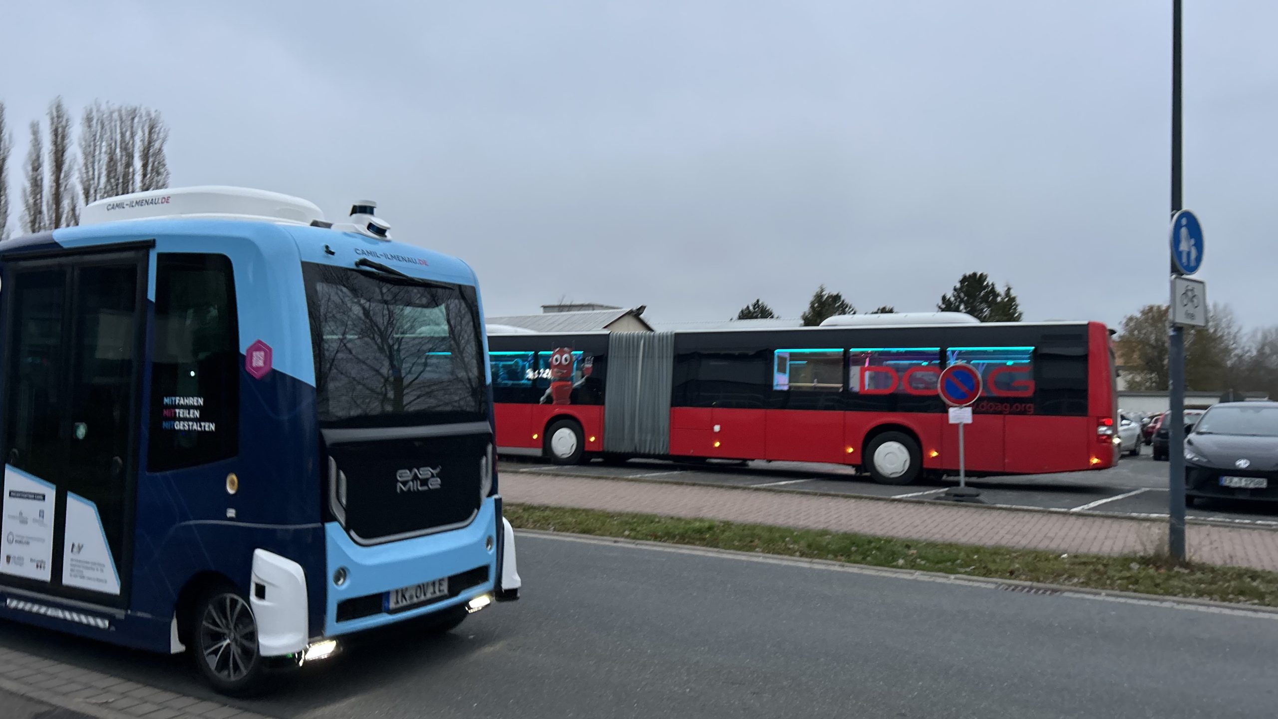 Ein kleiner Bus im Vordergrund und ein Gelenkzugbus im Hintergrund